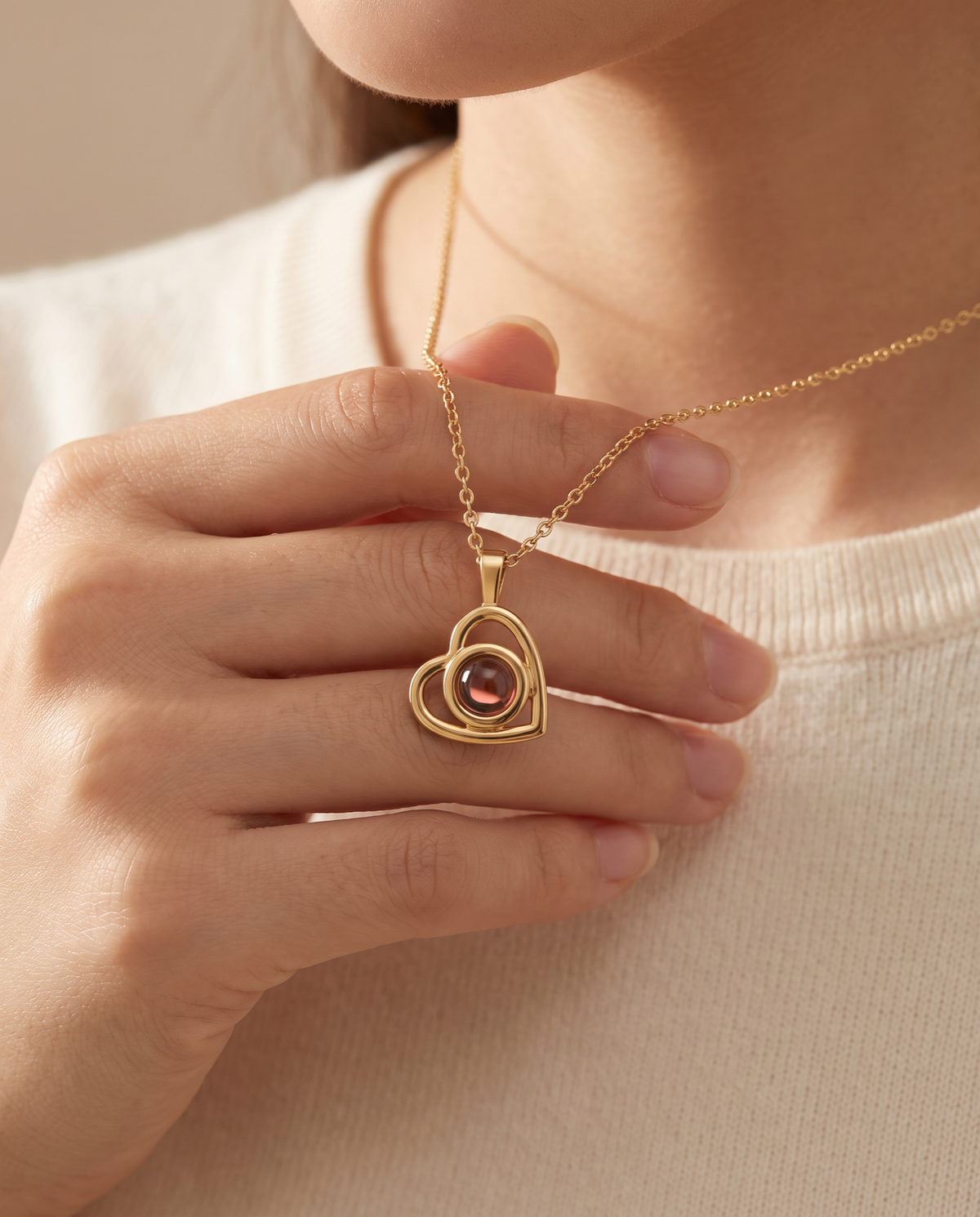 A woman holding the gold Hidden Photo pendant at her collarbone, the projection stone set in the heart